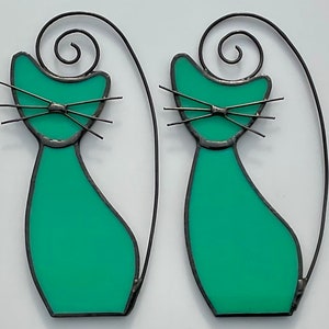 May include: Two teal blue stained glass cats with black wire outlines and curled tails. The cats have black wire whiskers and eyes.