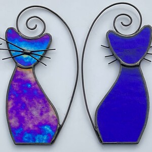 May include: Four stained glass cat figurines, two with a blue iridescent finish and two with a purple and blue iridescent finish. The cats are all in a standing pose with their tails curled over their backs.