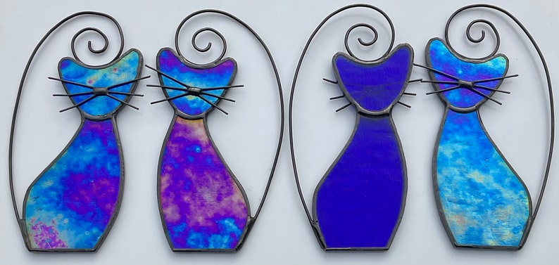 May include: Four stained glass cat figurines, two with a blue iridescent finish and two with a purple and blue iridescent finish. The cats are all in a standing pose with their tails curled over their backs.