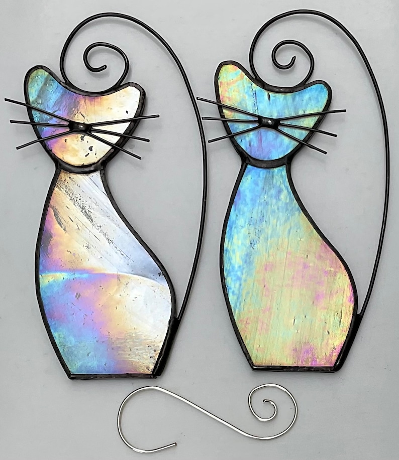 May include: Two iridescent glass cat ornaments with black wire frames and hanging loops. The cats are facing forward with their tails curled up behind them.