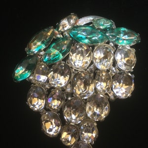 May include: A vintage brooch in the shape of a bunch of grapes. The grapes are made of clear rhinestones and the leaves are made of green rhinestones.