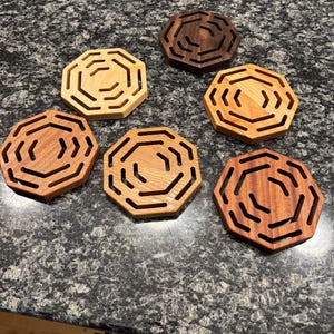 May include: Six octagonal wooden coasters with a geometric design. The coasters are made from different types of wood, including maple, walnut, and cherry.