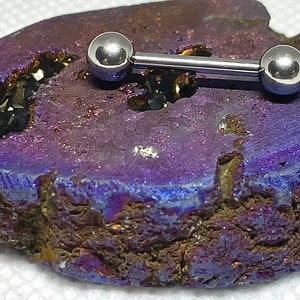 May include: A silver barbell with two round balls on each end. The barbell is resting on a purple and brown rock.