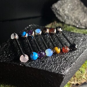 May include: A set of ten surgical steel barbell body jewelry with various gemstone ends. The gemstones include opal, amethyst, turquoise, tiger's eye, rose quartz, and onyx.