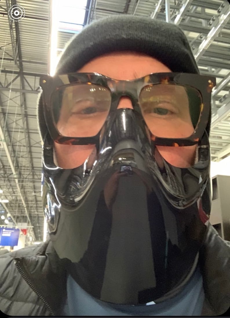 Op de afbeelding: Een persoon draagt ​​een zwart gezichtsmasker met een helder vizier en schildpadbril. De persoon draagt ​​een zwarte beanie en een zwart jack.