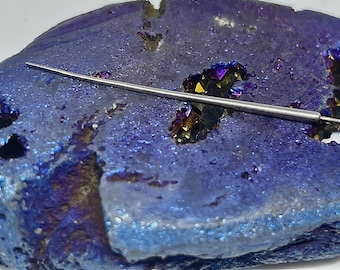 May include: A thin, silver, needle-like tool on a purple and gold iridescent agate geode.