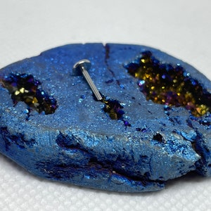 May include: A silver body piercing stud with a flat top, displayed on a blue and gold agate stone.