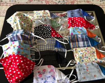 May include: A collection of 17 handmade face masks in various patterns and colors, including floral, plaid, polka dot, and geometric designs. The masks are made of fabric and have white elastic ear loops.