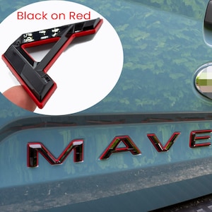 May include: Black and red "MAVERICK" lettering on the back of a blue truck. The letters are outlined in red and filled in black. The truck has a black and red emblem on the back.