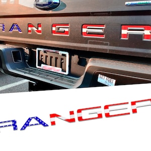 May include: A set of raised tailgate letters spelling RANGER, featuring a blue background with white stars on the R, and red and white horizontal stripes on the A, N, G, E, and R, designed to fit into the recessed lettering on a truck tailgate.