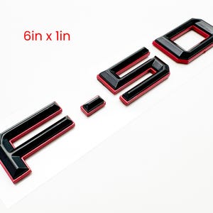 May include: Black and red automotive emblem with the text "F 40". The emblem is composed of individual letters and numbers, each outlined in red and filled with black. The dimensions are 6 inches by 1 inch.