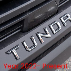 Peut inclure: Gros plan sur une calandre de camion Toyota Tundra noire avec le mot "Tundra" en lettres chromées. Année 2022 - Présent.