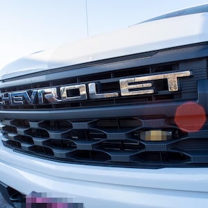 May include: Close-up of a white Chevrolet pickup truck with a black grille and the word "CHEVROLET" in chrome letters across the top.