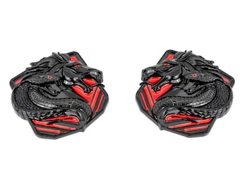 May include: A pair of black metal decorative emblems with a red and black geometric design. Each emblem features a stylized black horse head with a snake wrapped around its neck.