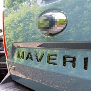 May include: A blue truck with a black "MAVERICK" emblem on the back. The truck has a chrome oval emblem with a green reflection.