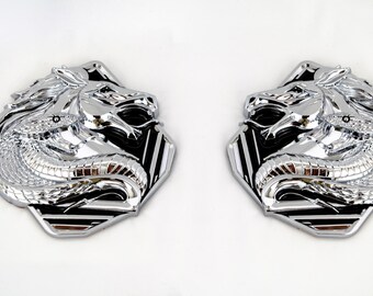 May include: A pair of silver-colored metal emblems featuring a horse and snake design. The emblems are in a hexagonal shape with a black and white striped pattern.