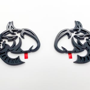 May include: Two black, stylised, 3D, abstract animal head emblems. The emblems are symmetrical and have a detailed, intricate design.