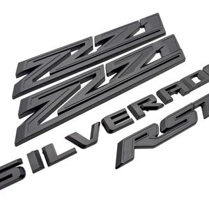 May include: Black automotive emblems for a Silverado truck. The set includes the letters "Z71", "SILVERADO", and "RST". The emblems are made of a matte black material and are arranged on a white background.