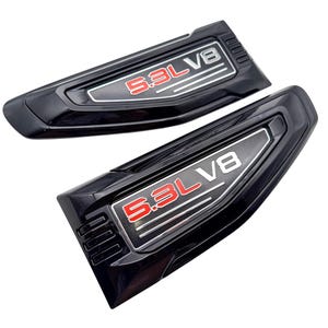 May include: Two black automotive emblems featuring a glossy finish with the text 5.3L V8 in red and silver lettering. Each badge has a tapered, angular shape with three horizontal lines and a textured border, designed for vehicle exterior mounting.