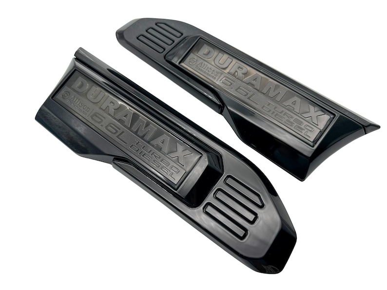 May include: Two black Duramax 6.6L Turbo Diesel engine covers. The covers are angled and have the Duramax logo and Allison 6.6L Turbo Diesel text embossed on them. The covers have a glossy finish.
