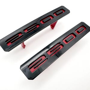 May include: Two black plastic emblems with red lettering that reads "2500".