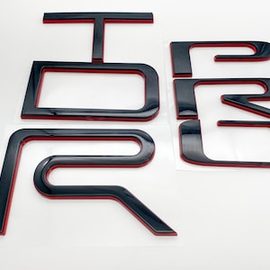 May include: Black and red 3D letters spelling out "FORD" with a red outline. The letters are raised and have a glossy finish.