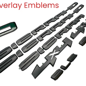 May include: A collection of black overlay emblems, including various shapes and sizes, arranged on a white background. The text "Overlay Emblems" is visible in red at the top. The emblems appear to be for automotive customization.