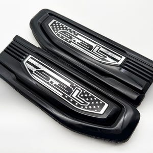 May include: Two black plastic emblems with a silver 3.3L inscription and an American flag design.