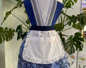 May include: A blue and white apron with a snowflake pattern and a white ruffled trim. The apron has a white pocket and a blue and white lace trim around the neck.