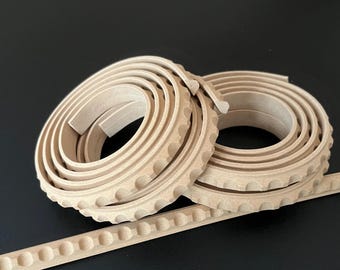 Könnte beinhalten: Beige dekorative Zierleistenrollen mit einem sich wiederholenden kreisförmigen Muster. Die Rollen sind aufgerollt, mit einem geraden Stück Zierleiste, das sich von den Rollen erstreckt. Der Hintergrund ist schwarz.
