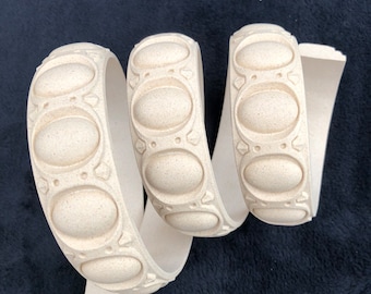 Könnte beinhalten: Eine beige Zierleiste mit einem sich wiederholenden Muster aus ovalen Formen. Die Leiste ist flexibel und kann verwendet werden, um Wänden, Möbeln oder anderen Oberflächen einen dekorativen Touch zu verleihen.