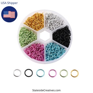 May include: A set of six containers filled with small jump rings in six different colors: gold, silver, black, green, pink, and blue. Each container has a separate compartment for each color. There are also six individual jump rings in the same colors, shown below the containers.