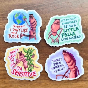 Puede incluir: Cuatro pegatinas caprichosas con una criatura rosa de dibujos animados y frases. Una pegatina dice: «Robert, no me gusta esta roca». Otra dice: «A veces es difícil ser un pequeño tipo como yo».
