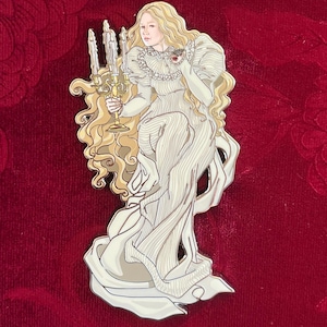 Puede incluir: Un pin de esmalte metálico que muestra a una persona con cabello rubio largo y ondulado, vestida con un traje blanco plisado de cuello alto. La figura sostiene un candelabro dorado con tres velas encendidas y tiene un pequeño detalle rojo.