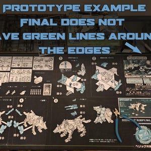 May include: A black surface displaying a model kit layout for a Command Wolf Zoids model, with diagrams and parts. The layout includes English and Japanese text, and a pair of blue-handled pliers. The text at the top reads "PROTOTYPE EXAMPLE".