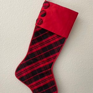 Könnte beinhalten: Roter und schwarzer karierter Weihnachtssocken mit roter Manschette und drei schwarzen Knöpfen.