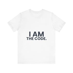 May include: A white short-sleeved t-shirt featuring the text I AM THE CODE. printed in dark gray capital letters across the center of the chest. The garment has a crew neckline and a standard fit, showcasing a clean and simple design.