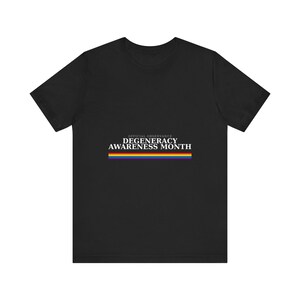 May include: A black short-sleeve t-shirt featuring the white text "OFFICIAL OBSERVANCE DEGENERACY AWARENESS MONTH" centered on the chest, positioned above a horizontal rainbow-colored stripe graphic that spans the width of the text.