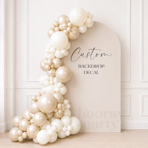 May include: An arched beige backdrop featuring the black text Custom BACKDROP DECAL and a large cluster of balloons in varying shades of cream, white, and metallic gold arranged along the left side and top of the arch structure.