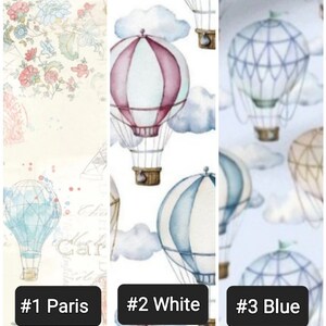 May include: Three different fabric patterns featuring hot air balloons. The first pattern is a light beige with a floral design. The second pattern is white with a light blue and pink hot air balloon design. The third pattern is light blue with a light blue and white hot air balloon design.