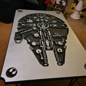Könnte beinhalten: Ein silberner Couchtisch mit einem schwarzen Millennium Falcon Design. Der Tisch hat einen schwarzen Metallrahmen.