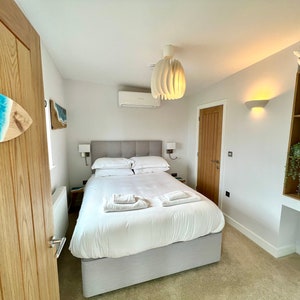 May include: A white bed with white linens and a gray headboard in a bedroom with white walls, a wooden door, and a white ceiling fan.