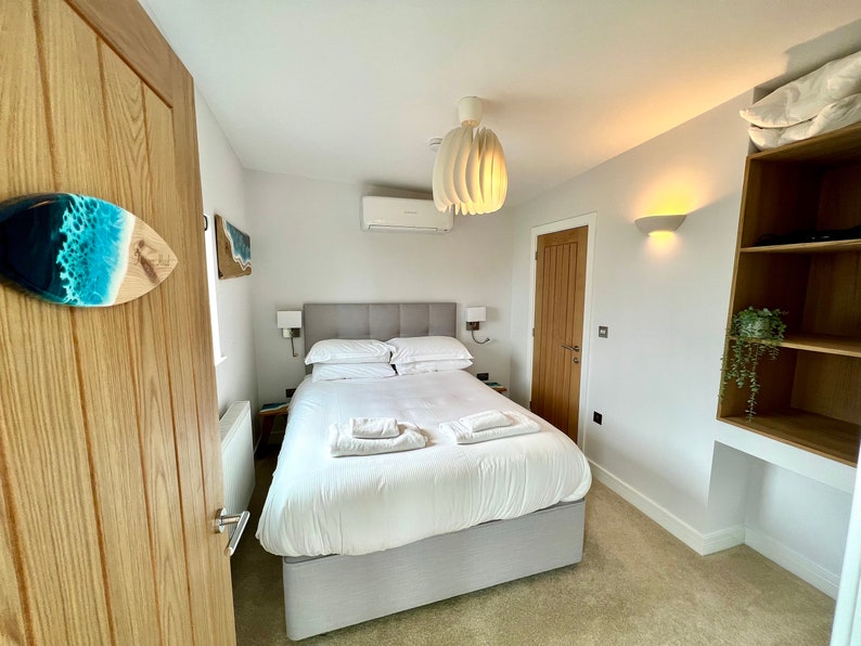 May include: A white bed with white linens and a gray headboard in a bedroom with white walls, a wooden door, and a white ceiling fan.