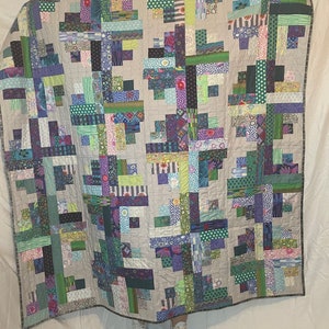 Könnte beinhalten: Ein Patchwork-Deckenstück mit einer Vielzahl von bunten Stoffen in Grün-, Lila- und Blautönen. Die Decke besteht aus Quadraten und Rechtecken, und die Stoffmuster sind geometrisch und floral.