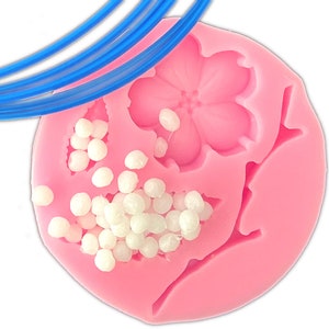 May include: Pink silicone mold with a flower and branch design. The mold is filled with white beads.