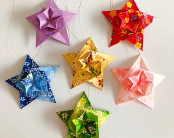 Puede incluir: Seis estrellas de origami con diferentes patrones y colores, incluyendo azul, rosa, verde, rojo y morado. Las estrellas están colgadas de cuerdas.