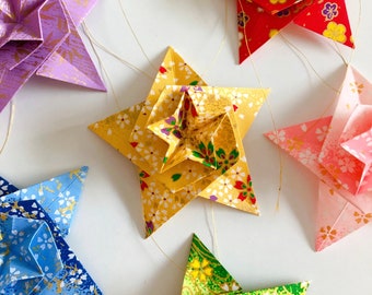 Puede incluir: Una colección de seis estrellas de origami, cada una con un papel estampado diferente. Las estrellas son de varios colores, incluyendo morado, amarillo, rosa, rojo y verde. Las estrellas están colgadas de cuerdas.