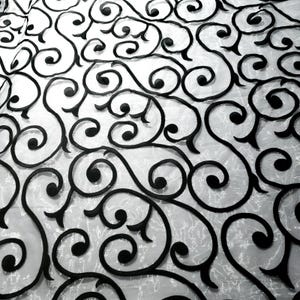 May include: Close-up of a white fabric with a repeating pattern of black, swirling, stylized floral designs. The black designs are raised and create a textured effect against the white background. The overall effect is elegant and decorative.