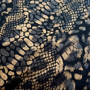 May include: Black fabric with a gold metallic snakeskin pattern. The pattern is made up of small, overlapping scales.