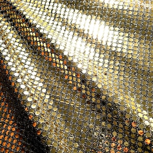 May include: Close-up of a shimmering gold fabric. The material is covered in small, round, reflective sequins, creating a textured surface. The sequins are arranged in a grid pattern, catching the light and creating a dazzling effect.